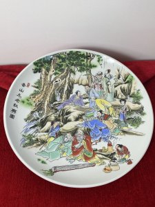 Large Porcelain Chinese Charger Plate With Ornate Celebratory Family Gathering Circa - 20th Century Vintage Composition - Porcelain Large Circular Decorative Porcelain Chinese Charger Plate With Hand Painted Scene Of A Intricate Family Celebratory Gathering Which Includes Twelve Figures Set Amongst Rocky Hillside Adorned With Oriental Trees. Some Figures Sit Playing Board Games, Reading Scriptures And Some Stand In Deep Conversation. A Young Female Carries A Laden Fruit Bowl Whilst Another Prepares Tea And Soup. Amazing Detail Of Finely Painted Faces, Hair And Hands With Wonderful Execution Of Oriental Costumes In Over Layered Fabric Kimonos And Fine Pattern In Bright Colours. Signed By Artist Front And Back. Dimensions In Inches Plate Diameter 13.5" Height From Table Top 1/2"