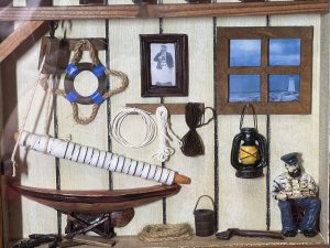 Intriguing Shipwright Diorama Model. Circa - Vintage Composition - Wood/Resin And Glass Unique Framed Diorama Model Of Shipwrights Workshop. Beamed Roof Workshop Display Showcasing Hoist Propping Up Ships Sails. Portrait Picture Set Upon The Wall Of Shipwright, The Actual Man In The Pictured Sits On A Chair With Ships Model In His Arms. An Array Of Shipping Rope Hangs On The Wall With Ships Lantern And Other Shipwright Tools. A Window View With Lighthouse In The Distance. Lovely Piece For Study Wall Of Nautical Enthusiast . Dimensions In Inches Height 11” Width 15”