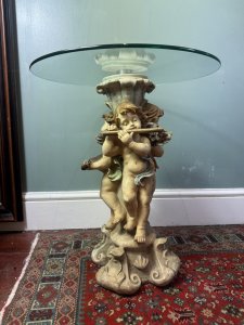 Trio of musical cherubs occasional table Composition - Resin and glass Circa - Vintage Listing Description Ornate table base comprised of entwined cherub figures each holding a different musical instrument (loot, harp, and flute) A richly coloured three dimensional piece with circular glass top. Dimensions in Cms Height 61cm X Top Width 50cm X Base Width 28cm