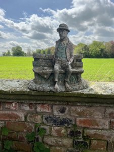 Wonderful Weathered Garden Showpiece Of Genius Albert Einstein Sitting Upon Wooden Bench. Bench Set Upon Rocky Base With Abundant Grassy Foliage Underneath. Albert Einstein March 14th 1879 - April 18th 1955.