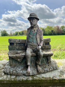 Wonderful Weathered Garden Showpiece Of Genius Albert Einstein Sitting Upon Wooden Bench. Bench Set Upon Rocky Base With Abundant Grassy Foliage Underneath. Albert Einstein March 14th 1879 - April 18th 1955.