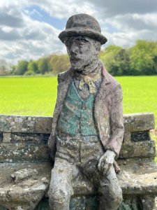 Wonderful Weathered Garden Showpiece Of Genius Albert Einstein Sitting Upon Wooden Bench. Bench Set Upon Rocky Base With Abundant Grassy Foliage Underneath. Albert Einstein March 14th 1879 - April 18th 1955.