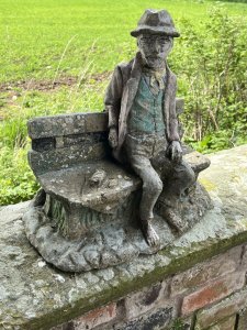 Wonderful Weathered Garden Showpiece Of Genius Albert Einstein Sitting Upon Wooden Bench. Bench Set Upon Rocky Base With Abundant Grassy Foliage Underneath. Albert Einstein March 14th 1879 - April 18th 1955.