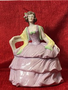 A Fashionable Elaborate Three Tiered Crinoline Gown With Bustier Bodice Decorated With Central Green Bow And Vibrant Yellow Scarf Placed Over Arms. Charming Details With Small Pointed Shoe Poking Out From Under The Gown.