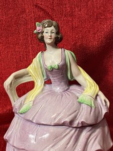 A Fashionable Elaborate Three Tiered Crinoline Gown With Bustier Bodice Decorated With Central Green Bow And Vibrant Yellow Scarf Placed Over Arms. Charming Details With Small Pointed Shoe Poking Out From Under The Gown.