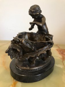Fine Reproduction French Bronze Cherub With Flora Urn Statue. Bronze Putti In Fine Detail Holding Flower Beside A Floral Urn Decorated With Forna Vines On A Oval Black Marble Base Exceptionally Ornate With Stunning Patina Composition- Bronze Dimensions Height 6 3/4” Width 5.5” Depth 4.5” Weight 3kg Approx
